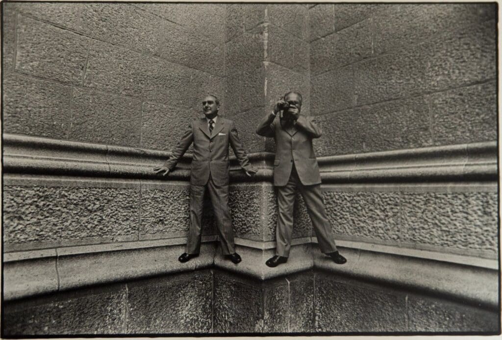 Two men standing on a wall with one man taking a picture.