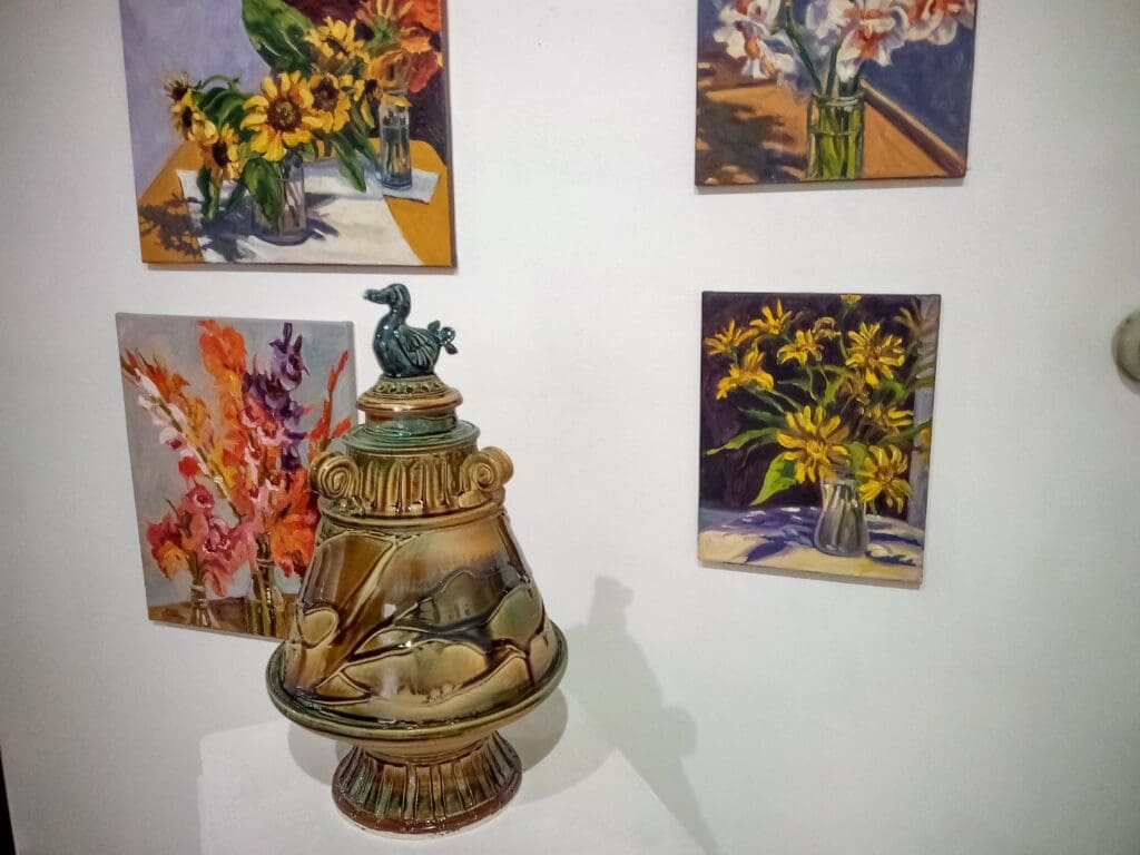 A vase with flowers on top of it next to paintings.