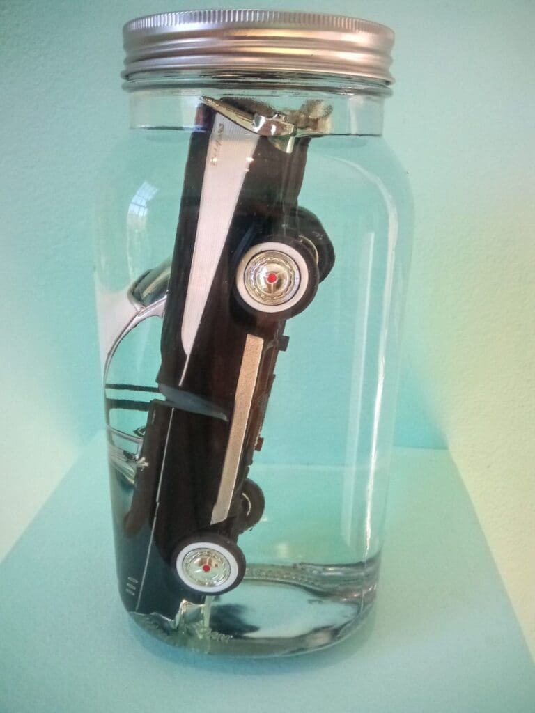 A car in a jar with a key chain attached.