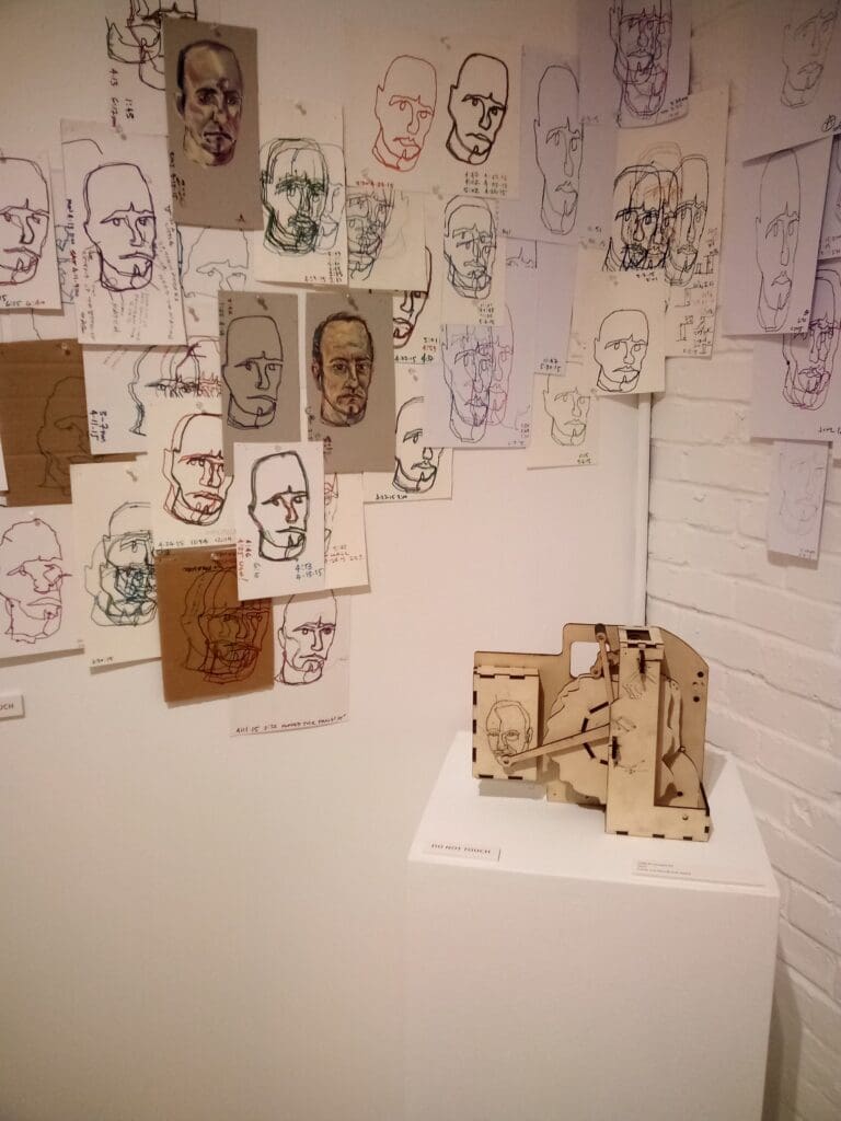 Wall of drawings with a wooden sculpture.