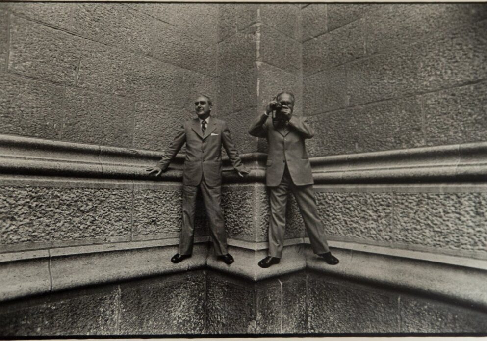 Two men standing on a wall with one man taking a picture.