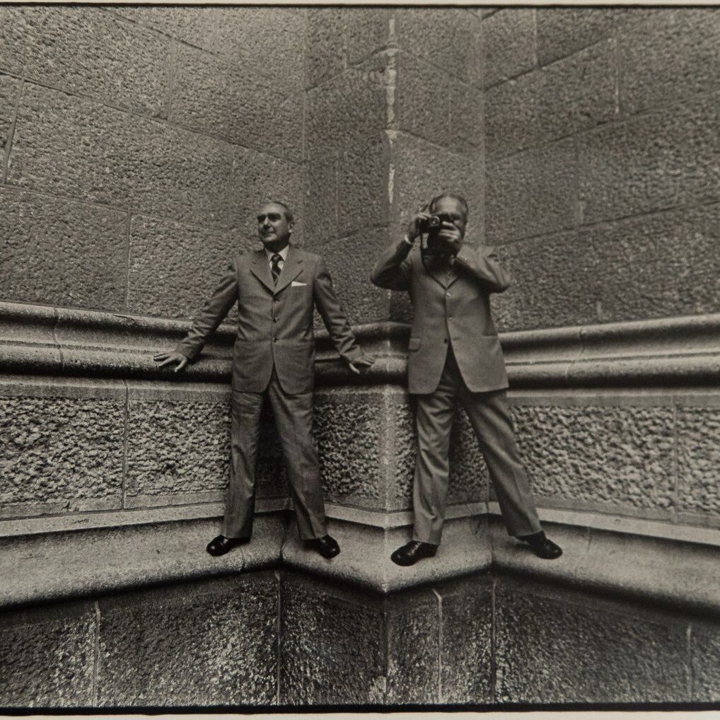 Two men standing on a wall with one man taking a picture.