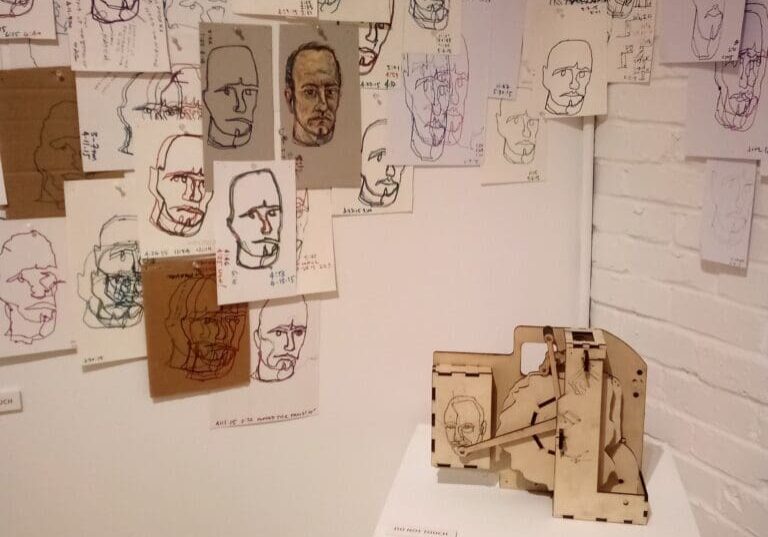 Wall of drawings with a wooden sculpture.