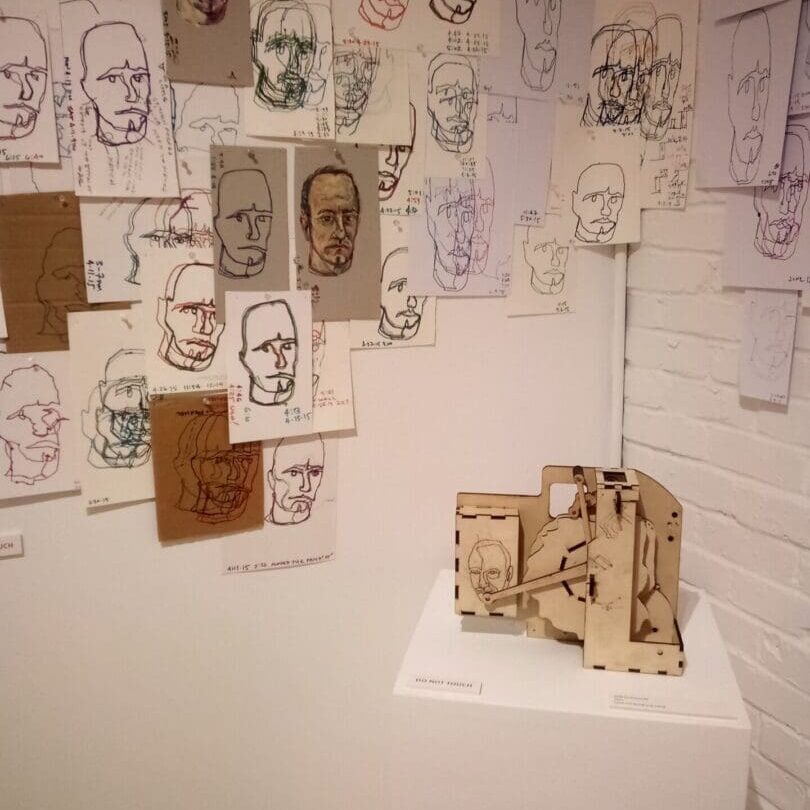 Wall of drawings with a wooden sculpture.