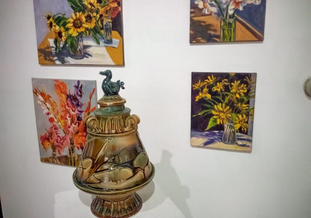 A vase with flowers on top of it next to paintings.