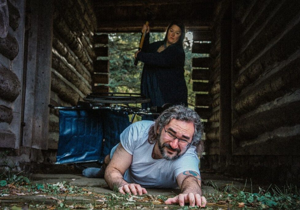 A man and woman in the woods with an ax.